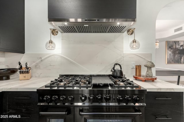 kitchen featuring backsplash, ventilation hood, light stone counters, range with gas stovetop, and dark cabinets