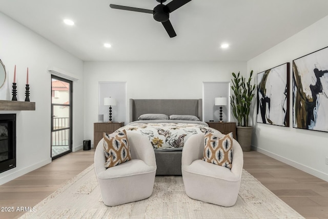 bedroom with a glass covered fireplace, recessed lighting, wood finished floors, and baseboards