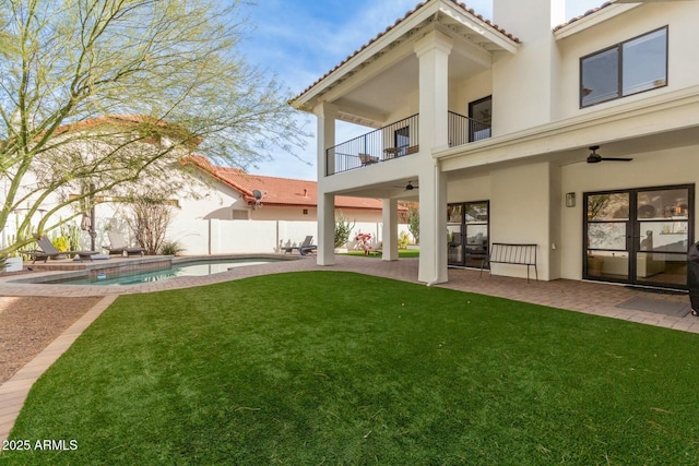 back of property with stucco siding, a lawn, a balcony, and ceiling fan