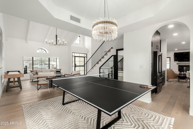 game room with visible vents, arched walkways, a notable chandelier, and light wood-style flooring