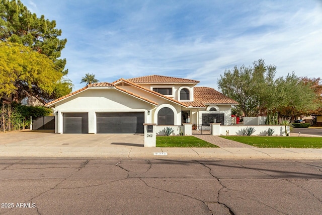 mediterranean / spanish house with stucco siding, driveway, a tile roof, a fenced front yard, and a garage