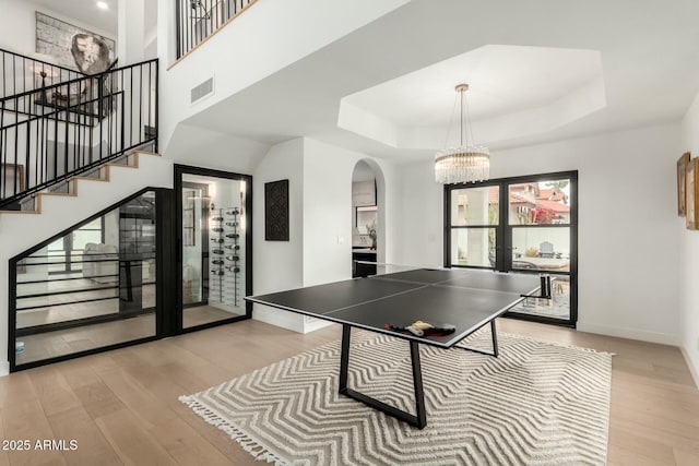 game room with visible vents, a tray ceiling, light wood-style flooring, arched walkways, and french doors