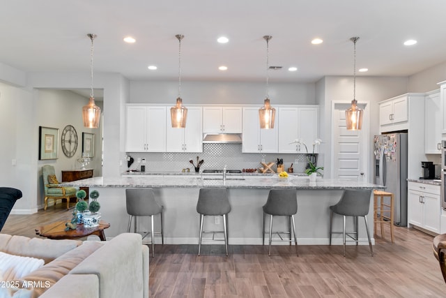 kitchen featuring stainless steel fridge, a kitchen island with sink, hanging light fixtures, and white cabinets