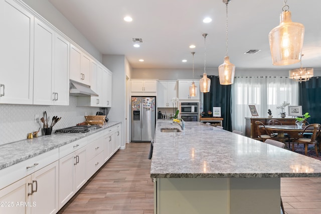 kitchen featuring white cabinetry, decorative light fixtures, stainless steel appliances, and a large island with sink