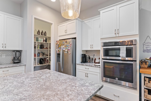 kitchen with pendant lighting, tasteful backsplash, white cabinets, and appliances with stainless steel finishes