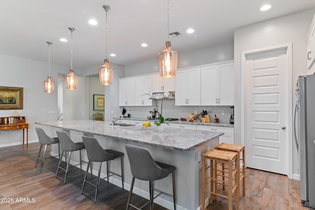 kitchen with light wood-type flooring, freestanding refrigerator, white cabinetry, and backsplash