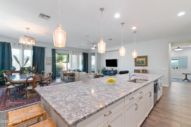 kitchen with light stone counters, a sink, visible vents, white cabinetry, and decorative light fixtures