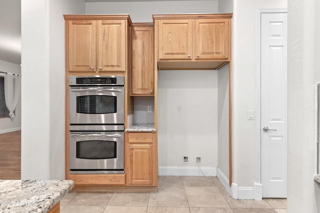 kitchen featuring light tile patterned floors, light stone countertops, double oven, and backsplash