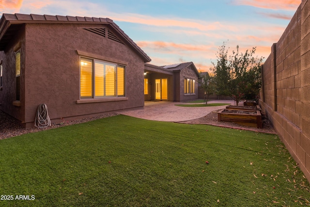 back house at dusk featuring a patio and a lawn