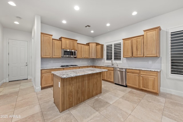 kitchen featuring sink, appliances with stainless steel finishes, a center island, light stone counters, and tasteful backsplash