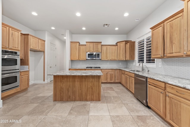 kitchen featuring a kitchen island, tasteful backsplash, sink, stainless steel appliances, and light stone countertops