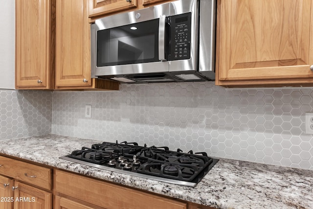 kitchen featuring decorative backsplash, light stone countertops, and appliances with stainless steel finishes