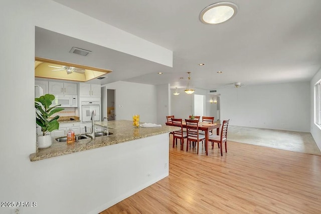 kitchen with light wood-type flooring, white appliances, ceiling fan, white cabinets, and a peninsula