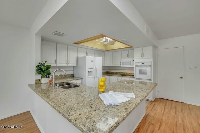 kitchen with light wood-type flooring, white appliances, a sink, ceiling fan, and a peninsula