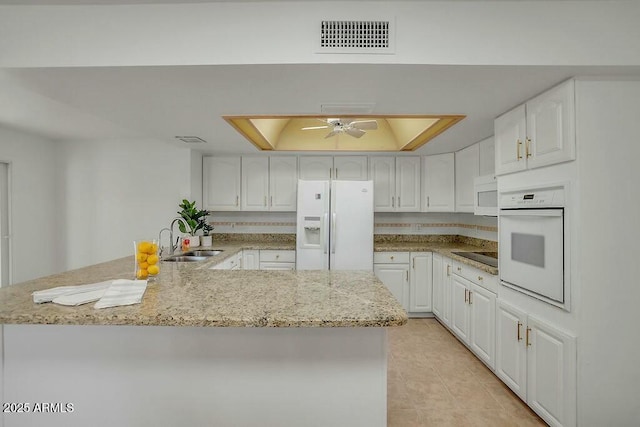 kitchen featuring white cabinets, visible vents, white appliances, a sink, and a tray ceiling