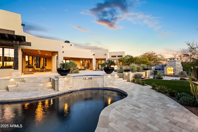 pool at dusk with a fireplace and a patio