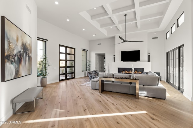 living room with coffered ceiling, beam ceiling, light hardwood / wood-style flooring, and a high ceiling