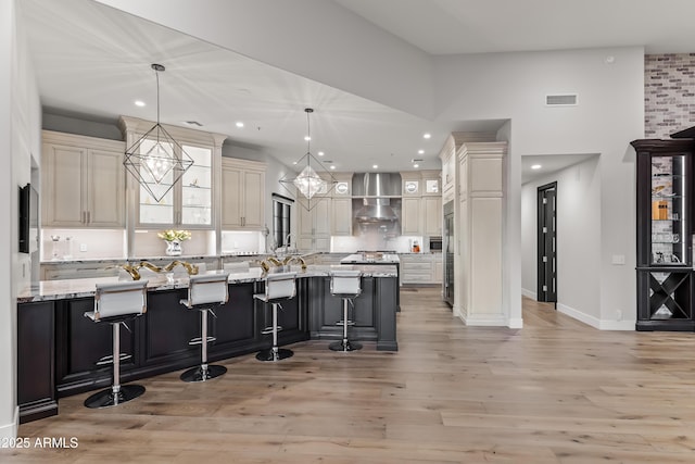 kitchen featuring pendant lighting, wall chimney exhaust hood, a large island, and a breakfast bar area