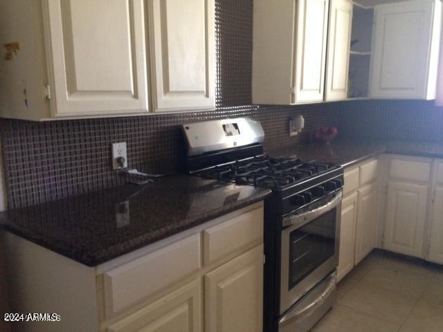 kitchen with decorative backsplash, white cabinetry, light tile patterned floors, and stainless steel range with gas stovetop