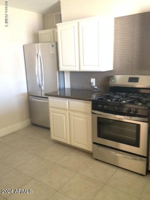 kitchen featuring white cabinets, light tile patterned floors, white refrigerator, and stainless steel gas range