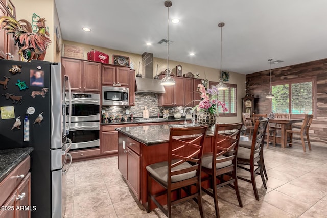 20962 W Thomas Rd, Buckeye, AZ 85396 - kitchen featuring stainless steel appliances, wall chimney exhaust hood, tasteful backsplash, a kitchen island with sink, and wooden walls