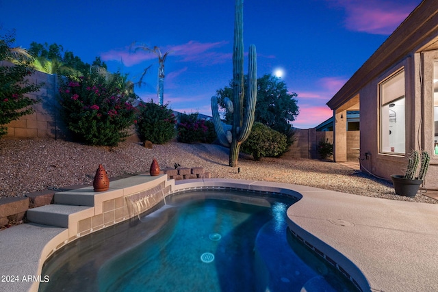 pool at dusk featuring a jacuzzi and fence