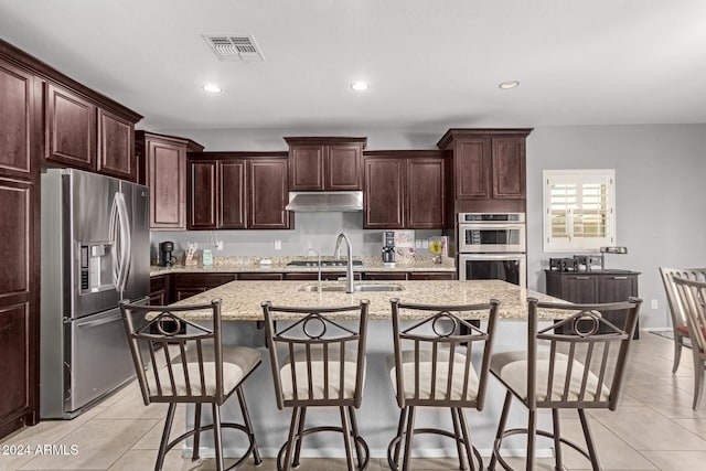 kitchen with light stone counters, light tile patterned floors, an island with sink, and appliances with stainless steel finishes