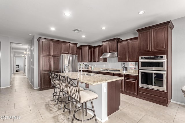 kitchen with a kitchen bar, light stone countertops, stainless steel appliances, sink, and an island with sink