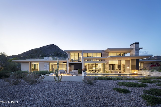 4451 E Joshua Tree Ln, Paradise Valley, AZ 85253 - back of property at dusk with a patio area, a mountain view, an outdoor pool, and an outdoor living space with a fire pit