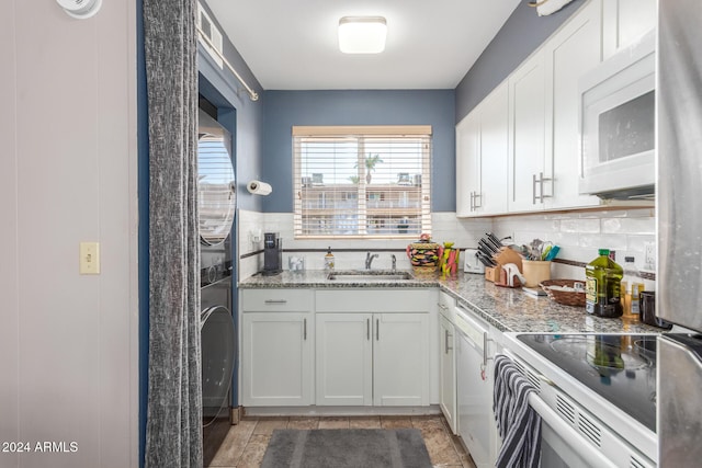 kitchen with light stone countertops, white cabinetry, stacked washer and clothes dryer, and sink