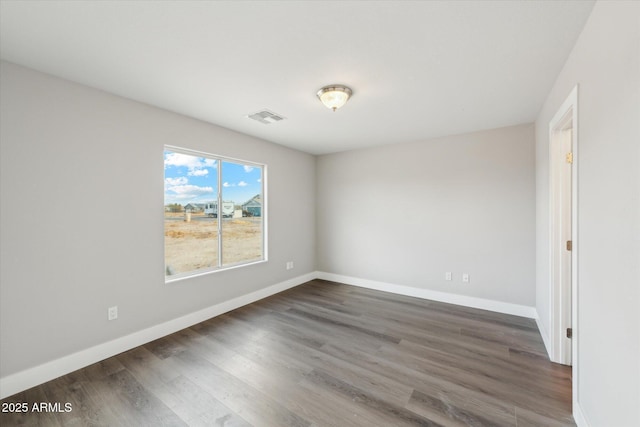 empty room featuring wood finished floors, visible vents, and baseboards