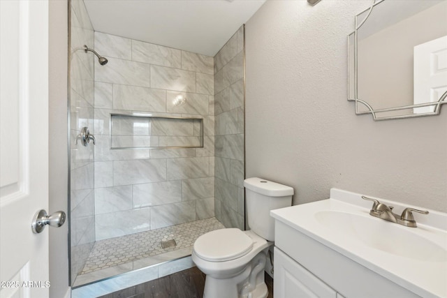 full bathroom featuring a textured wall, a tile shower, vanity, and toilet