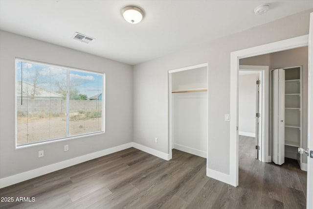 unfurnished bedroom with a closet, visible vents, dark wood finished floors, and baseboards