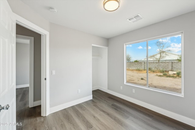 unfurnished bedroom with baseboards, a closet, visible vents, and wood finished floors