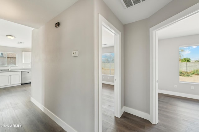 hallway featuring wood finished floors, a sink, visible vents, and baseboards