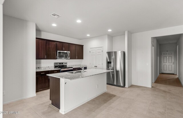 5053 S 252nd Ave, Buckeye, AZ 85326 - kitchen featuring appliances with stainless steel finishes, dark brown cabinetry, an island with sink, a sink, and light stone counters