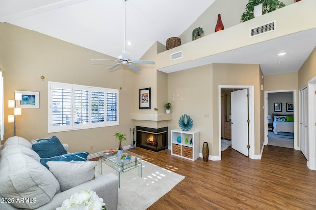 living room featuring a multi sided fireplace, ceiling fan, a towering ceiling, and hardwood / wood-style flooring