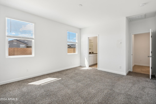 unfurnished bedroom featuring light carpet, ensuite bath, visible vents, and baseboards