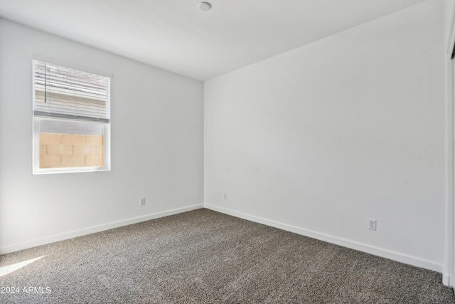 spare room featuring dark colored carpet and baseboards