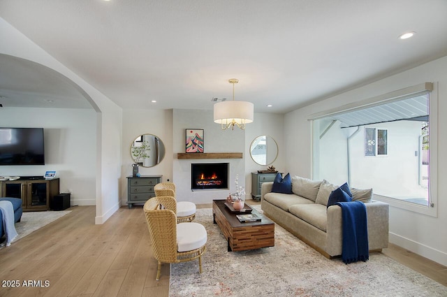 living area featuring visible vents, arched walkways, baseboards, a lit fireplace, and light wood-style floors