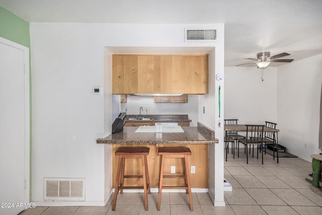 kitchen featuring kitchen peninsula, a kitchen bar, ceiling fan, sink, and light tile patterned floors