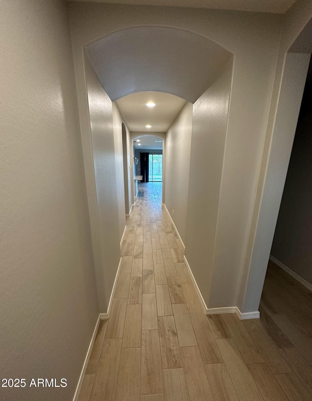 hall with arched walkways, baseboards, and wood finish floors
