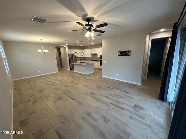unfurnished living room featuring arched walkways, ceiling fan with notable chandelier, light wood finished floors, and visible vents