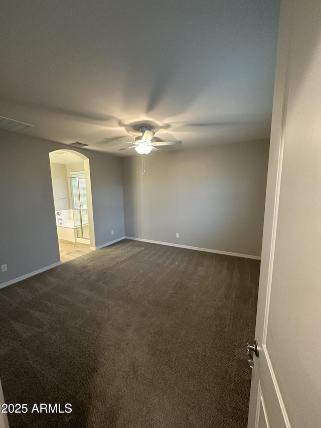 carpeted empty room featuring visible vents, ceiling fan, arched walkways, and baseboards