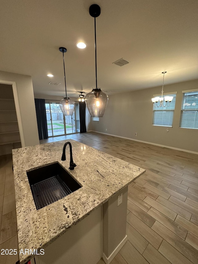 kitchen featuring wood finished floors, a sink, light stone countertops, and hanging light fixtures