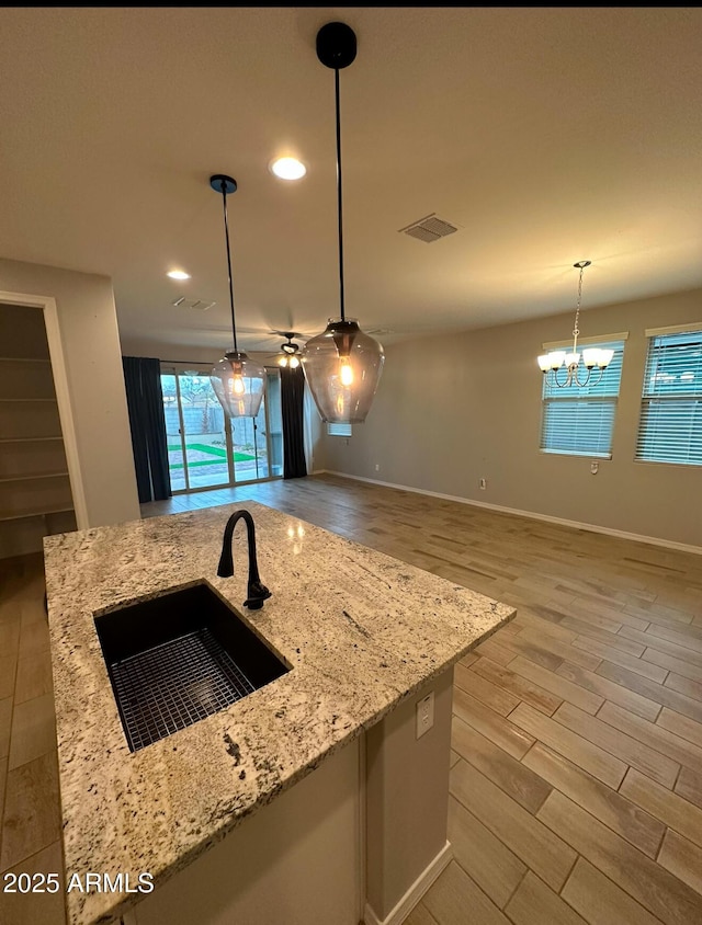 kitchen with visible vents, decorative light fixtures, a sink, light wood finished floors, and light stone counters