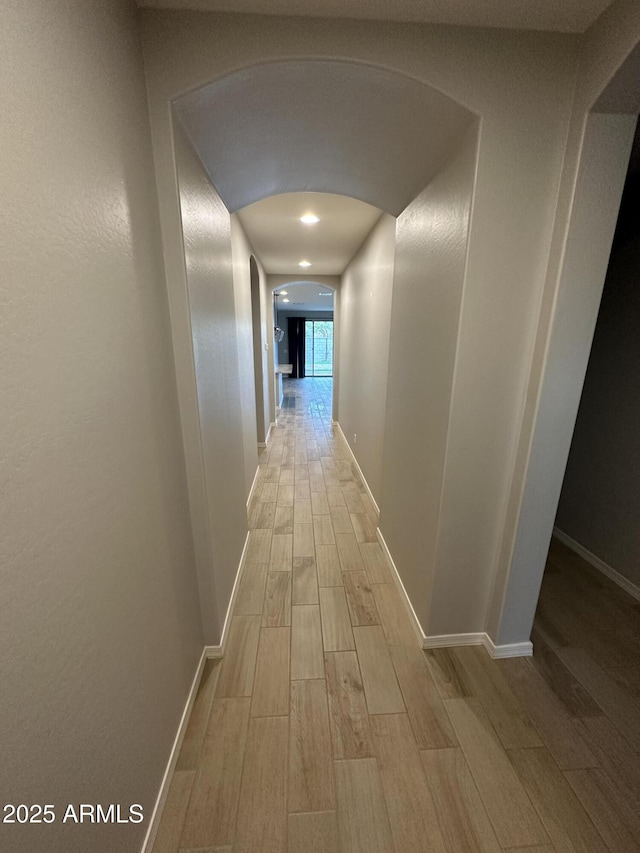 corridor featuring arched walkways, baseboards, and wood tiled floor