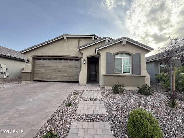 ranch-style home featuring a tiled roof, a garage, stucco siding, and decorative driveway