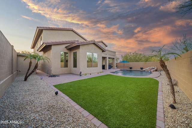 back house at dusk featuring a patio, a fenced in pool, and a lawn