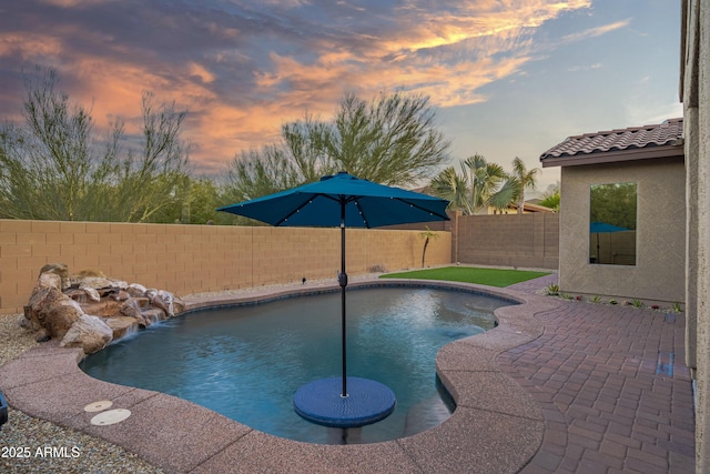 pool at dusk with a patio area and pool water feature